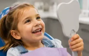 Smiling child holding a tooth model during a pediatric restorative dental care visit.